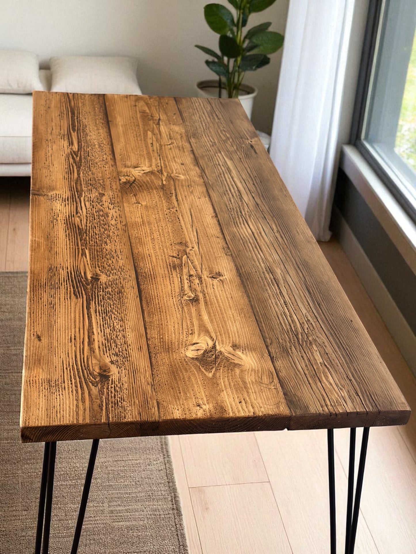 Wooden desk with black legs in a room with a couch and plant